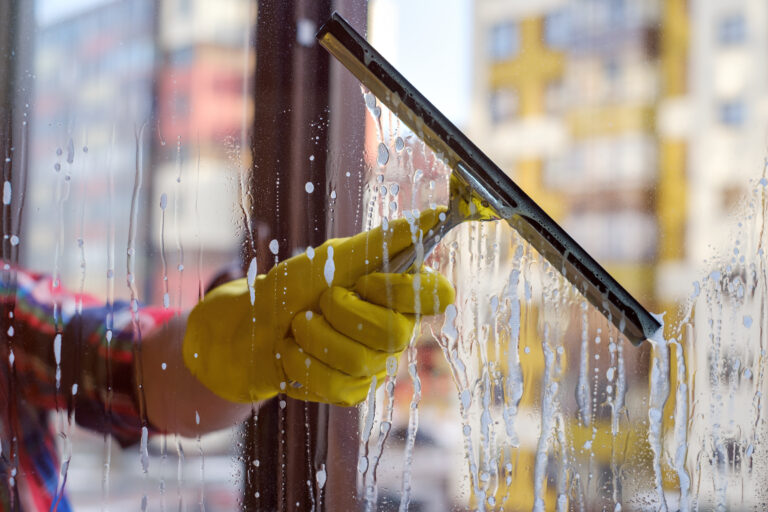 Scraper for washing windows in hands in yellow gloves. Wash the dirty and dusty windows in the spring